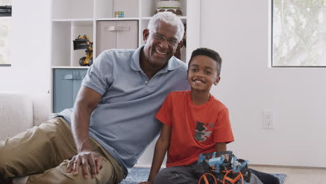 Portrait-Of-Grandfather-With-Grandson-Sitting-On-Rug-At-Home-Building-Model-Helicopter-Together