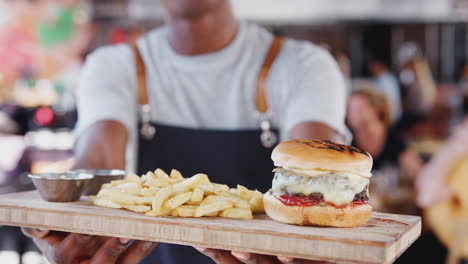 Close-Up-Of-Waiter-Serving-Burger-And-Fries-In-Busy-Bar-Restaurant