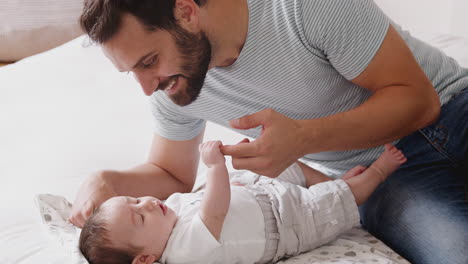 Close-Up-Of-Loving-Father-Playing-With-Newborn-Baby-Son-Lying-On-Bed-At-Home-In-Loft-Apartment