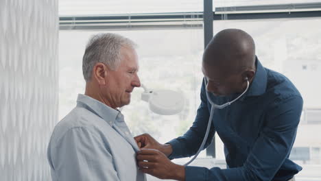 Médico-Escuchando-A-Un-Paciente-Masculino-Mayor-Respirando-Con-Estetoscopio-Durante-El-Examen-Médico-En-El-Consultorio