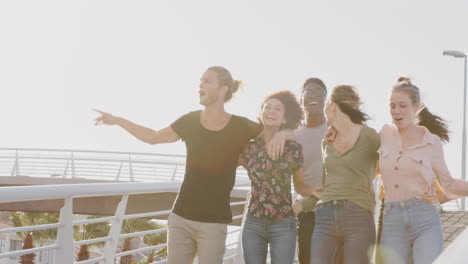 Group-Of-Young-Friends-Outdoors-Walking-Across-Bridge-Together-Against-Flaring-Sun