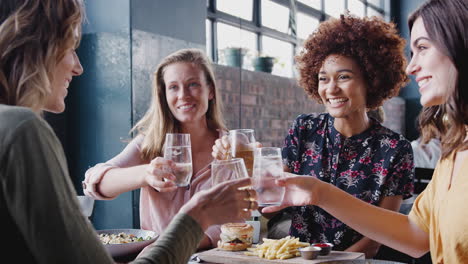 Four-Young-Female-Friends-Meeting-For-Drinks-And-Food-Making-A-Toast-In-Restaurant