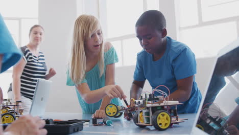 Two-Students-With-Female-Teacher-In-After-School-Computer-Coding-Class-Learning-To-Program-Robot-Vehicle