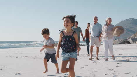 Multi-Generation-Family-Walking-Along-Sandy-Beach-On-Summer-Vacation