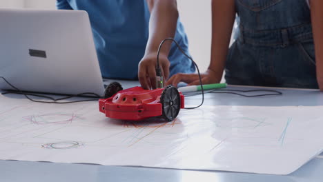 Primer-Plano-De-Dos-Estudiantes-Programando-Un-Vehículo-Robot-En-Una-Clase-De-Codificación-Informática-Después-De-La-Escuela