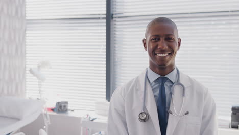 Portrait-Of-Male-Doctor-Wearing-White-Coat-With-Stethoscope-Standing-In-Front-Of-Desk-In-Office