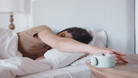Woman-Asleep-In-Bed-Reaches-Out-To-Turn-Off-Alarm-Clock-On-Bedside-Table