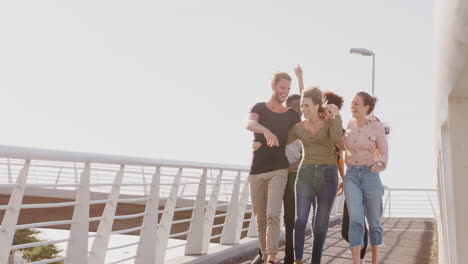 Group-Of-Young-Friends-Outdoors-Walking-Across-Bridge-Together-Against-Flaring-Sun