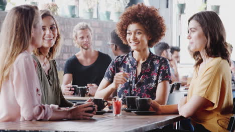 Four-Young-Female-Friends-Meeting-Sitting-At-Table-In-Coffee-Shop-And-Talking