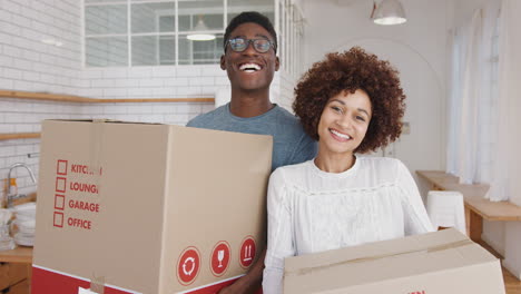 Portrait-Of-Smiling-Young-Couple-Carrying-Boxes-Into-New-Home-On-Moving-Day