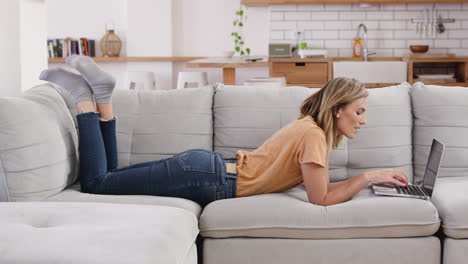 Woman-Relaxing-Lying-On-Sofa-At-Home-Working-On-laptop