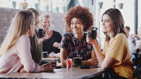 Four-Young-Female-Friends-Meeting-Sitting-At-Table-In-Coffee-Shop-And-Talking