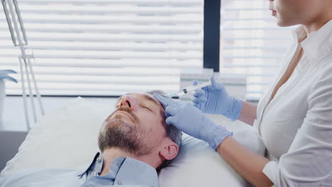 Kosmetikerin-Gibt-Einem-Reifen-Männlichen-Patienten-Eine-Botox-Injektion-In-Die-Stirn