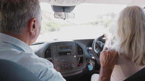 Interior-View-Of-Senior-Couple-On-Vacation-Driving-Hire-Car-Along-Country-Road