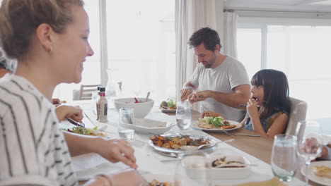 Mehrgenerationenfamilie-Sitzt-Zu-Hause-Am-Tisch-Und-Isst-Gemeinsam