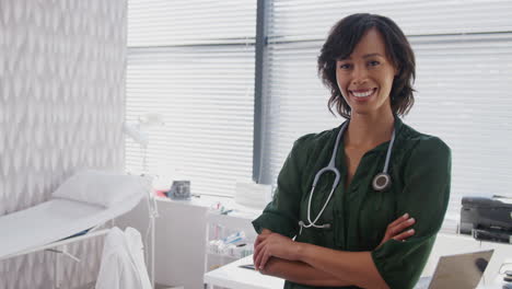 Portrait-Of-Smiling-Female-Doctor-With-Stethoscope-Standing-In-Front-Of-Desk-In-Office