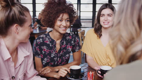 Four-Young-Female-Friends-Meeting-Sitting-At-Table-In-Coffee-Shop-Talking
