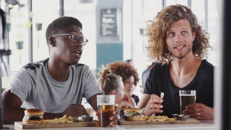 Two-Male-Friends-Eating-Food-And-Drinking-Beer-In-Sports-Bar