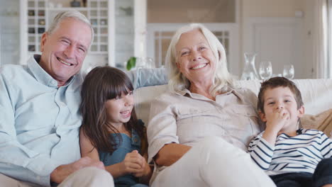 Porträt-Lächelnder-Großeltern,-Die-Mit-Enkelkindern-Zu-Hause-Auf-Dem-Sofa-Sitzen