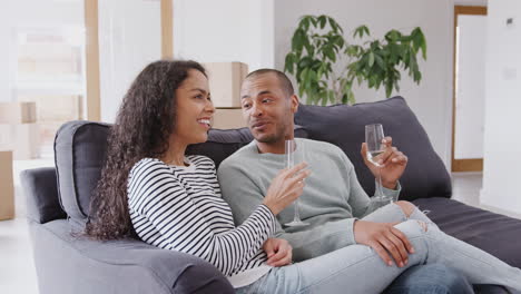 Couple-Taking-A-Break-And-Sitting-On-Sofa-Celebrating-Moving-Into-New-Home-With-Champagne