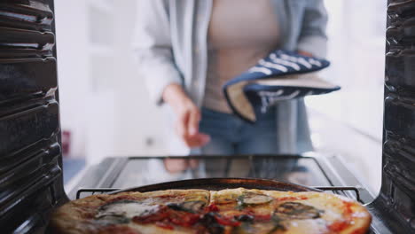 Blick-Aus-Dem-Inneren-Des-Ofens,-Während-Eine-Frau-Frische-Pizza-Kocht