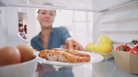 Young-Woman-Reaching-Inside-Refrigerator-Of-Healthy-Food-For-Fresh-Salmon-On-Plate