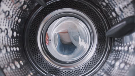Blick-Aus-Dem-Inneren-Der-Waschmaschine,-Während-Eine-Frau-Die-Weiße-Wäscheladung-Hineinnimmt