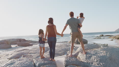Family-On-Summer-Vacation-Standing-On-Rocks-Looking-Out-To-Sea