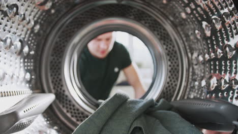 Blick-Aus-Dem-Inneren-Der-Waschmaschine,-Während-Der-Mann-Wäscheladung-Hineinlegt