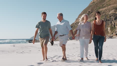 Ältere-Eltern-Mit-Erwachsenen-Nachkommen,-Die-Im-Sommerurlaub-Am-Sandstrand-Entlang-Spazieren