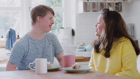 Young-Downs-Syndrome-Couple-Enjoying-Tea-And-Cake-In-Kitchen-At-Home