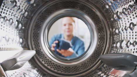 Blick-Aus-Dem-Inneren-Der-Waschmaschine,-Während-Eine-Frau-Wäscheladung-Hineinlegt