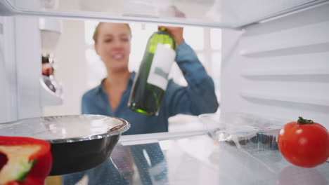 Mujer-Joven-Metiendo-Dentro-Del-Refrigerador-Y-Sacando-Una-Botella-De-Vino-Y-Comida-Preparada.
