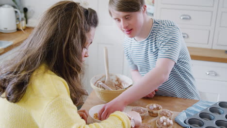 Junges-Down-Syndrom-Paar-Dekoriert-Hausgemachte-Cupcakes-Mit-Marshmallows-In-Der-Heimischen-Küche