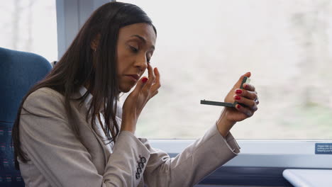 Mujer-De-Negocios-Sentada-En-El-Tren-Viajando-Al-Trabajo-Maquillándose-Usando-Un-Espejo