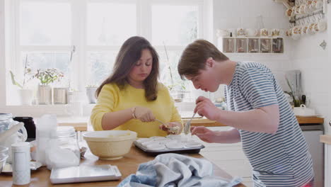 Young-Downs-Syndrome-Couple-Putting-Mixture-Into-Paper-Cupcake-Cases-In-Kitchen-At-Home