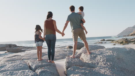 Family-On-Summer-Vacation-Standing-On-Rocks-Looking-Out-To-Sea