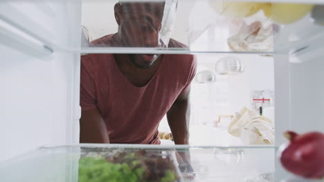 Blick-Aus-Dem-Inneren-Des-Kühlschranks,-Während-Ein-Mann-Die-Tür-öffnet-Und-Eine-Einkaufstüte-Mit-Lebensmitteln-Auspackt