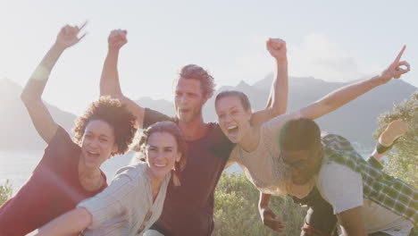 Men-Lifting-Up-Women-As-Group-Of-Friends-Have-Fun-Against-Flaring-Sun