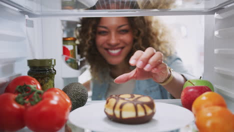 View-Looking-Out-From-Inside-Of-Refrigerator-As-Woman-Opens-Door-And-Reaches-For-Unhealthy-Donut
