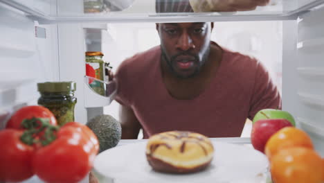 View-Looking-Out-From-Inside-Of-Refrigerator-As-Man-Opens-Door-And-Reaches-For-Unhealthy-Donut