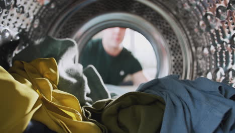 Blick-Aus-Dem-Inneren-Der-Waschmaschine,-Während-Ein-Mann-Wäsche-Herausnimmt