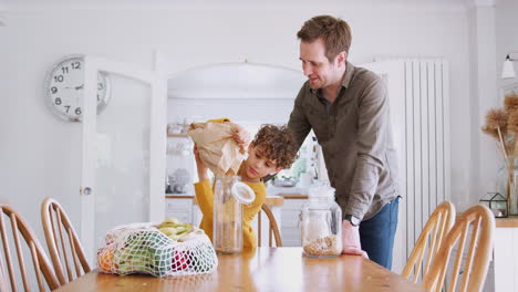Vater-Hilft-Sohn-Beim-Nachfüllen-Von-Lebensmittelbehältern-Zu-Hause-Mit-Zero-Waste-Verpackungen