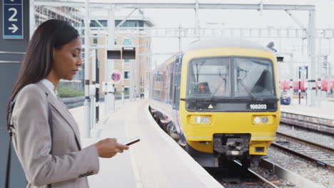 Businesspeople-Commuting-To-Work-Standing-On-Train-Platform-Using-Mobile-Phone-As-Train-Arrives