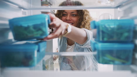 Blick-Aus-Dem-Inneren-Des-Kühlschranks,-Während-Eine-Frau-Ein-Gesundes-Lunchpaket-Aus-Einem-Behälter-Herausnimmt