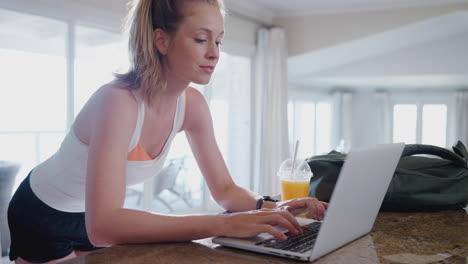 Young-Woman-Downloading-Data-From-Personal-Health-Tracker-To-Laptop-After-Exercise