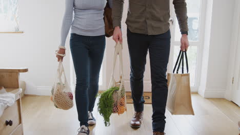 Close-Up-Of-Couple-Returning-Home-From-Shopping-Trip-Carrying-Groceries-In-Plastic-Free-Bags