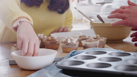 Nahaufnahme-Eines-Down-Syndrom-Paares,-Das-In-Der-Heimischen-Küche-Hausgemachte-Cupcakes-Mit-Marshmallows-Dekoriert