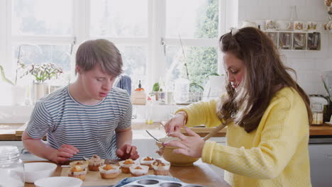 Junges-Down-Syndrom-Paar-Dekoriert-Hausgemachte-Cupcakes-Mit-Zuckerguss-In-Der-Heimischen-Küche