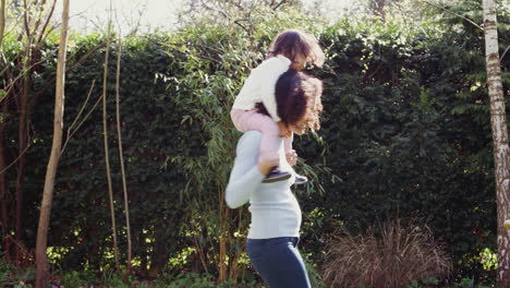 Mother-Giving-Young-Daughter-Ride-On-Shoulders-In-Garden-At-Home
